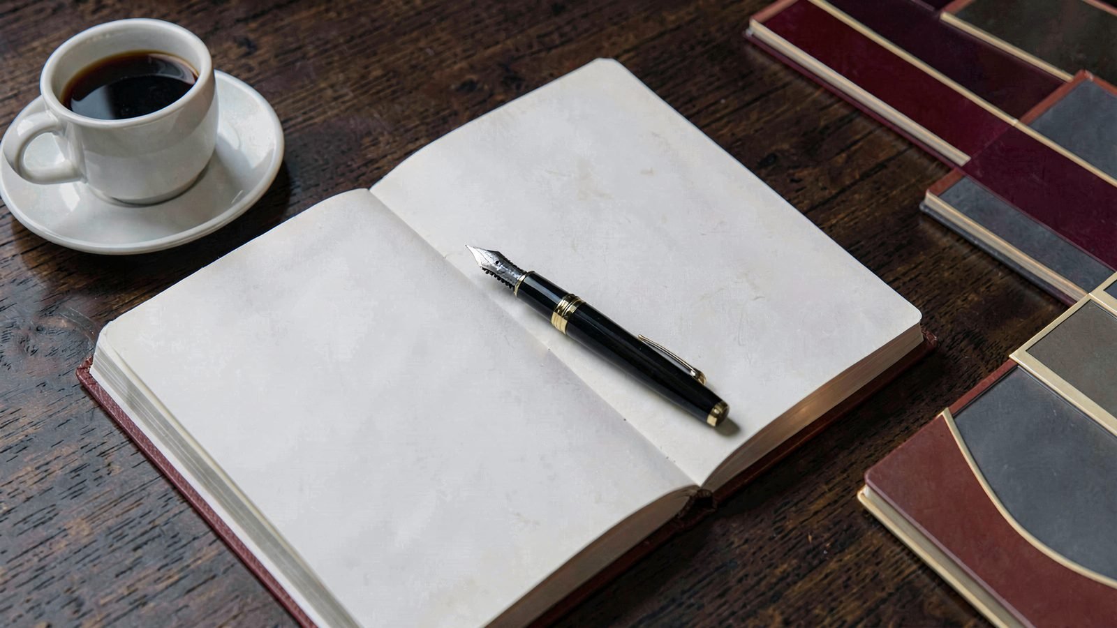 Fotografía ilustrativa: cuaderno abierto con pluma y café sobre un escritorio de madera